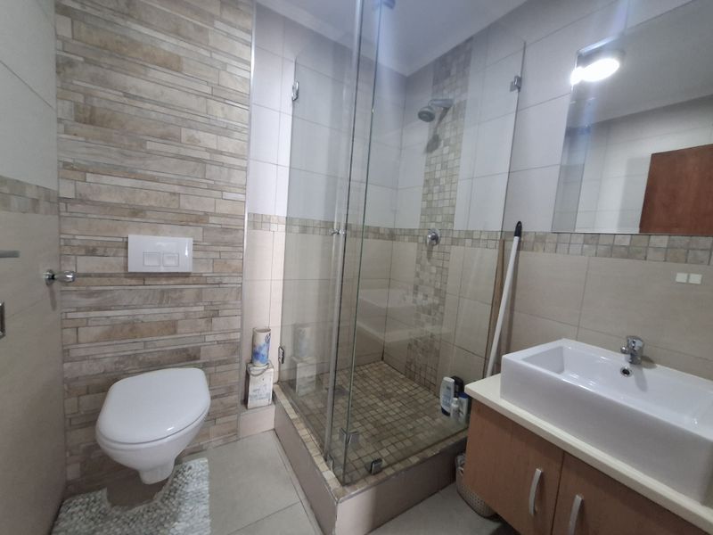 Modern bathroom featuring a wall-mounted toilet, a glass-enclosed shower with mosaic tile accents, and a vanity unit with a basin.