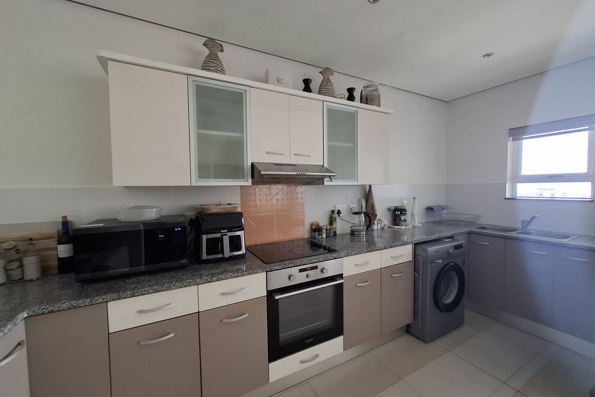 A functional kitchen featuring two-tone cabinetry, granite countertops, integrated oven and hob, and tiled flooring with space for a washing machine.