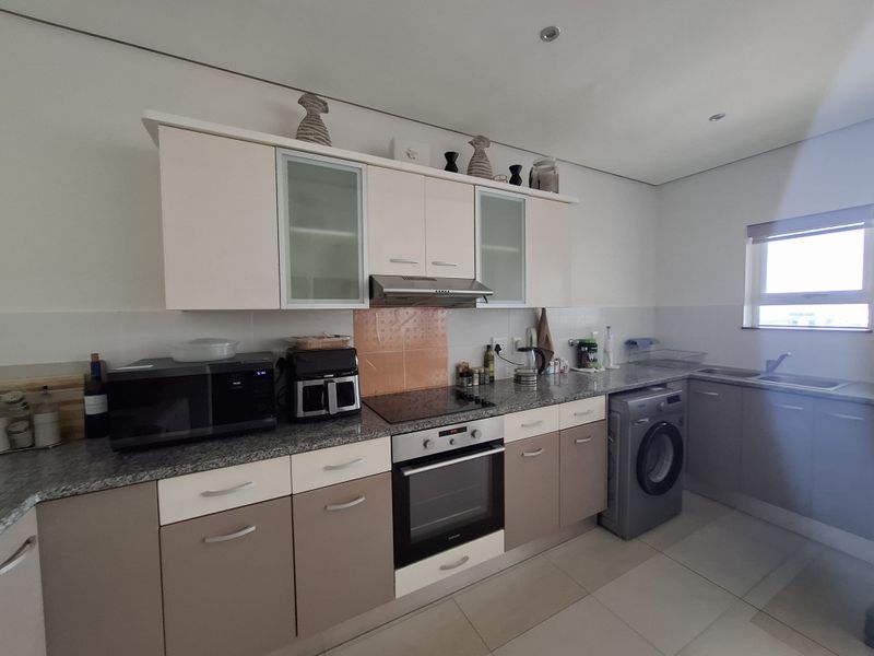 A functional kitchen featuring two-tone cabinetry, granite countertops, integrated oven and hob, and tiled flooring with space for a washing machine.