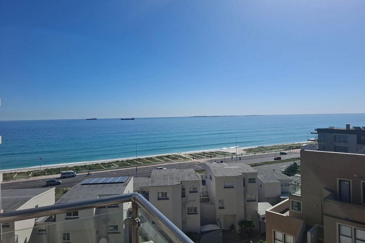 A clear, elevated view of the ocean and coastline from a balcony with a modern glass balustrade.