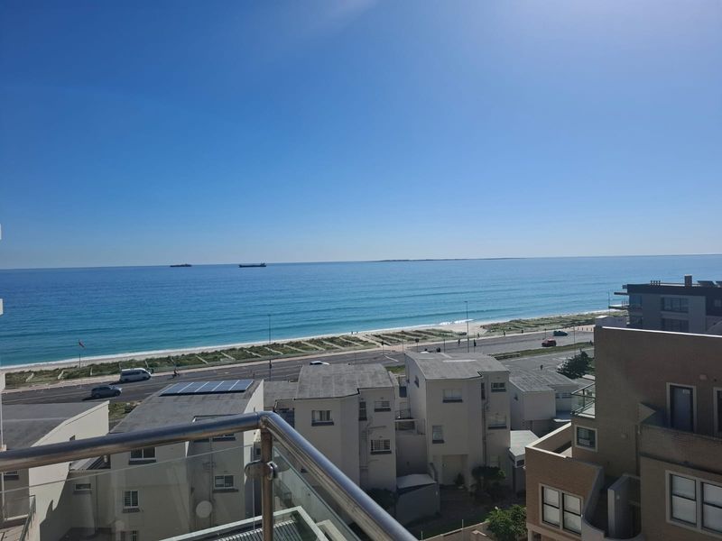 A clear, elevated view of the ocean and coastline from a balcony with a modern glass balustrade.