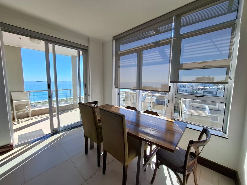 Bright dining area featuring large windows with roller blinds and sliding glass doors leading to a balcony with ocean views.