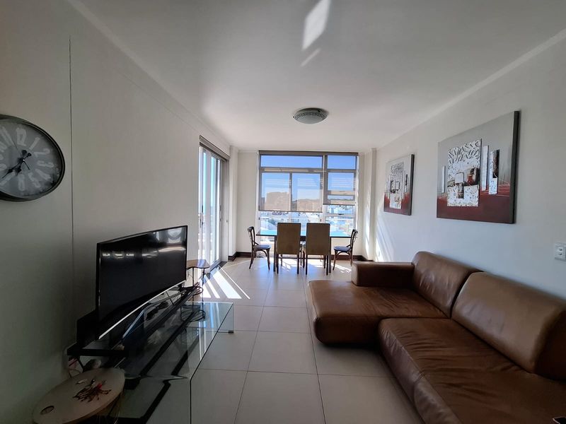 Bright open-plan living and dining area featuring large windows, tiled flooring, and direct access to a balcony through sliding glass doors.