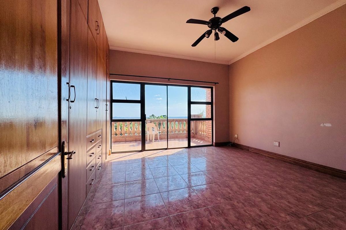 Spacious bedroom featuring built-in wooden cupboards, tiled flooring, a ceiling fan, and large sliding glass doors opening onto a private balcony with scenic views.