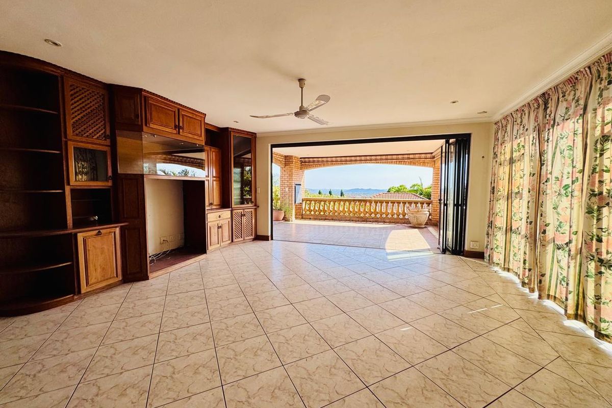 Spacious living area featuring built-in wooden cabinetry, tiled flooring, and large folding doors opening onto a covered balcony with scenic views.