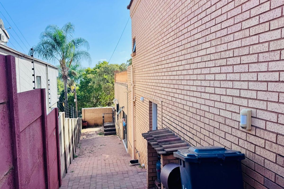 A side exterior walkway featuring brick paving, brick wall construction, and perimeter security fencing.