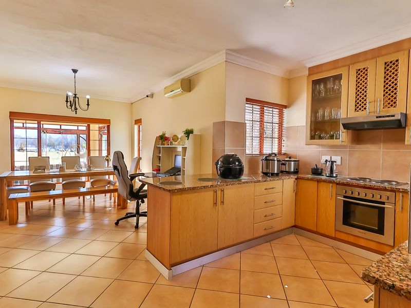Open-plan kitchen and dining area featuring granite countertops, wooden cabinetry, built-in appliances, and tiled flooring, creating a functional and connected living space.