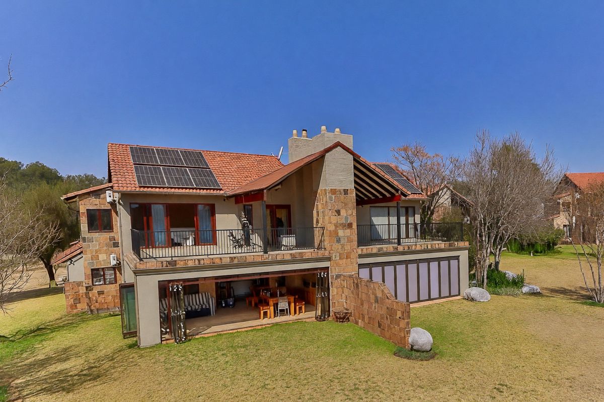 Rear view of a multi-level townhouse featuring stone cladding, terracotta roof tiles, solar panels, a spacious balcony, and a covered patio with stacking doors.