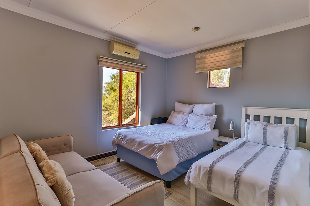 A well-lit bedroom featuring neutral wall tones, timber-framed windows with roller blinds, and a wall-mounted split-system air conditioning unit.