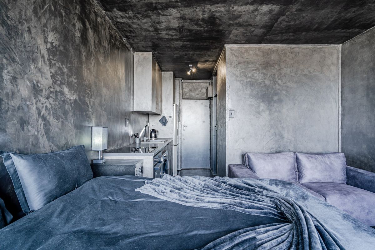 Modern open-plan studio apartment featuring industrial-style concrete finishes, a compact kitchenette with integrated appliances, and a cohesive living and sleeping area.