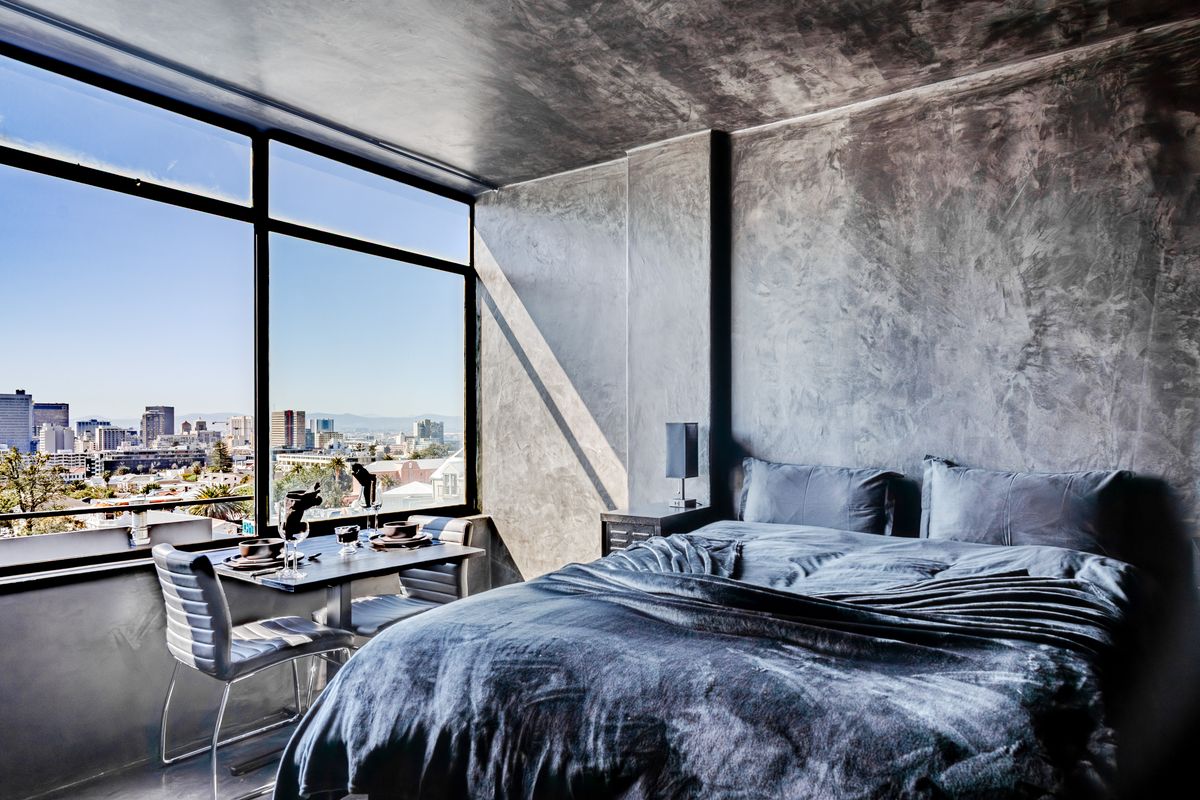 Modern bedroom featuring high-end polished concrete wall finishes and expansive floor-to-ceiling windows offering panoramic city views.