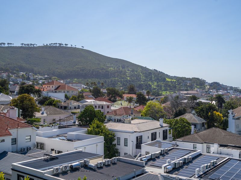 An elevated view overlooking a residential neighborhood with mountain vistas, featuring rooftops equipped with solar panels and air conditioning units.