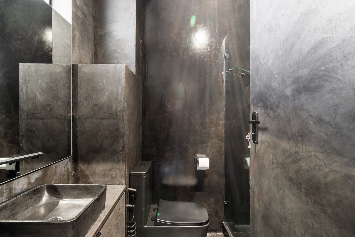 Modern bathroom featuring dark cementitious wall finishes, a sleek vessel sink, and a minimalist toilet and shower area.