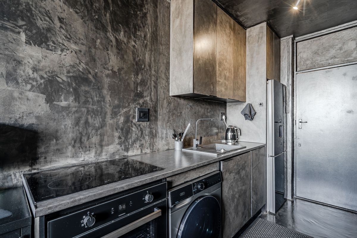 Modern industrial-style kitchen featuring concrete-look cabinetry, built-in oven, electric hob, and integrated laundry facilities with a sleek, minimalist aesthetic.