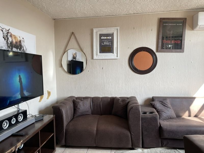A living room featuring tiled flooring and a wall-mounted air conditioning unit, currently decorated with various wall hangings.