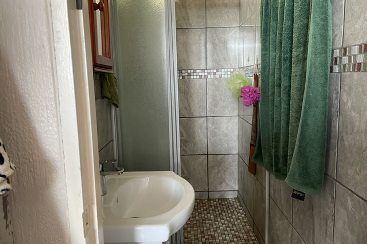 Compact bathroom featuring a pedestal washbasin and a tiled shower enclosure with mosaic flooring.
