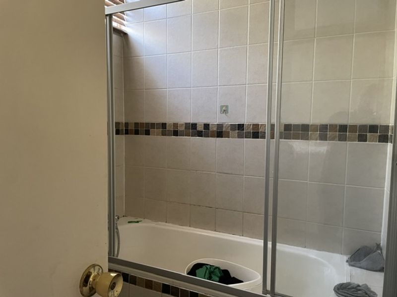A functional bathroom featuring a built-in bathtub with a glass shower screen and neutral wall tiling with a decorative mosaic accent border.
