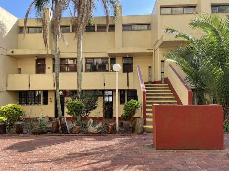 Front elevation of a multi-level townhouse complex featuring brick paving, concrete staircases, and balconies with established landscaping.