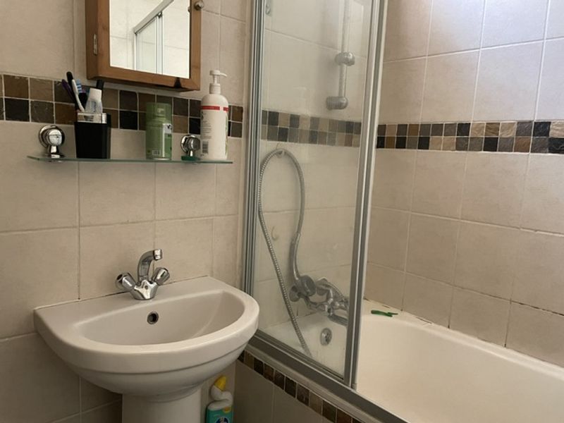 A functional bathroom featuring a pedestal basin, a bathtub with an integrated shower screen, and tiled wall finishes with a decorative border.