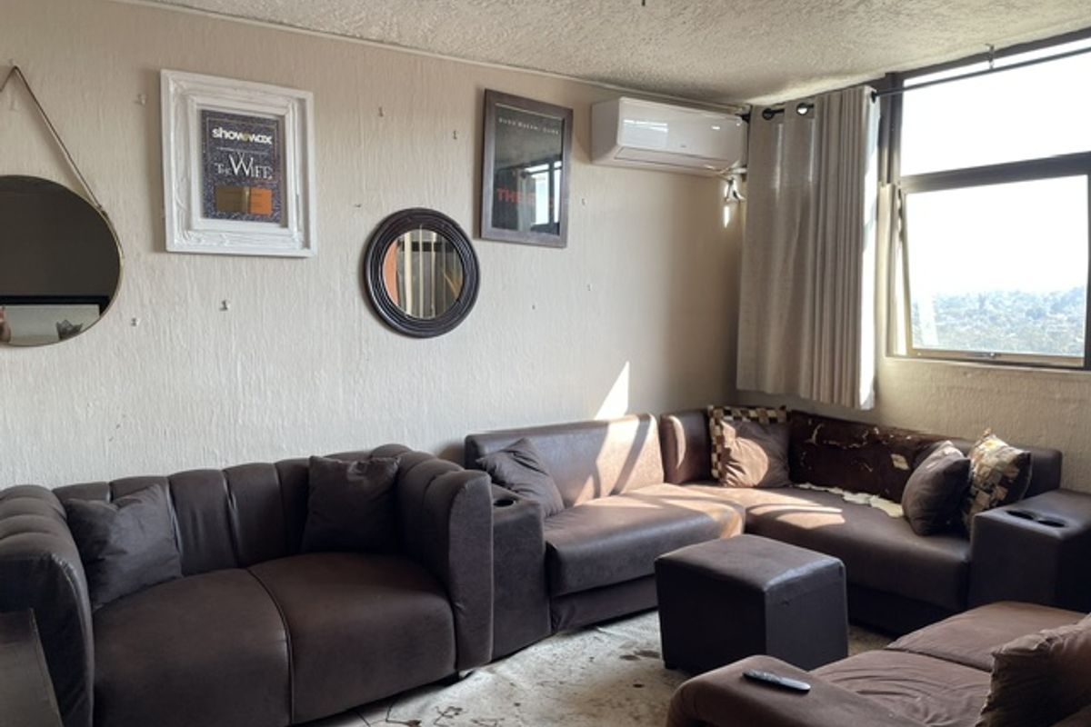 A living room featuring tiled flooring, an air conditioning unit, and a large window providing natural light.