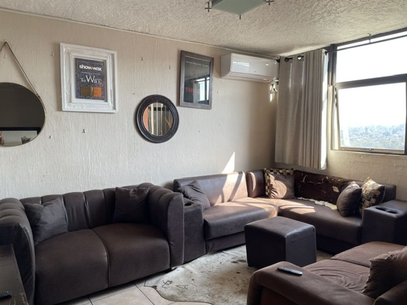 A living room featuring tiled flooring, an air conditioning unit, and a large window providing natural light.
