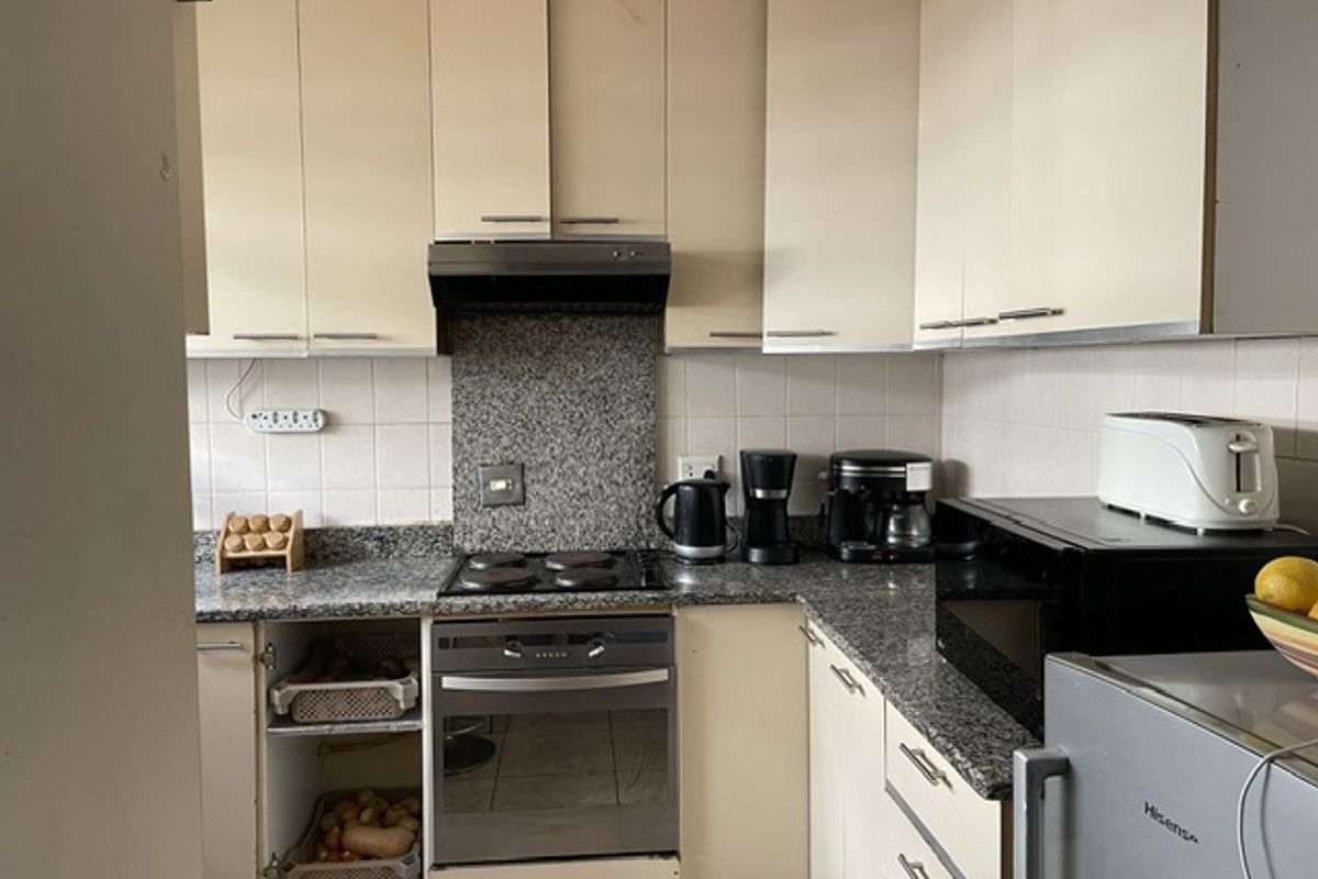 A compact kitchen featuring granite countertops, built-in cabinetry, and integrated appliances, currently showing signs of wear and requiring cosmetic updates.