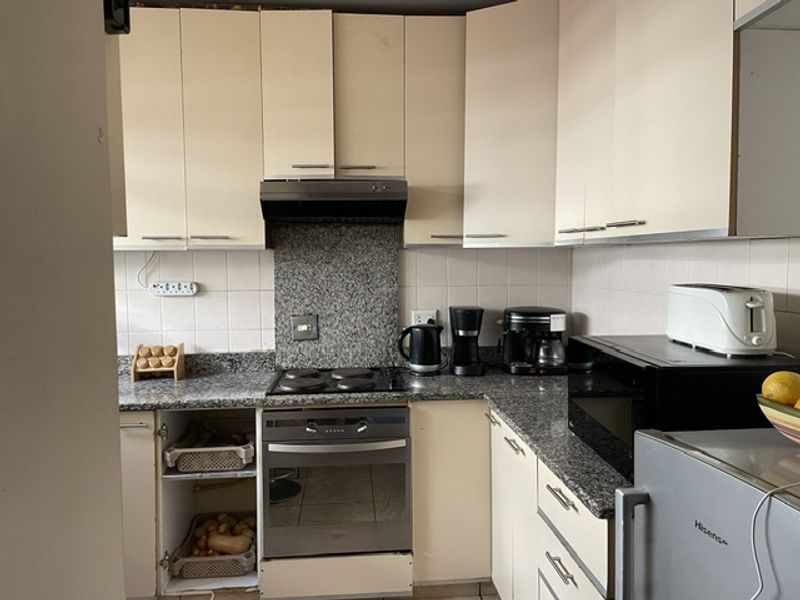 A compact kitchen featuring granite countertops, built-in cabinetry, and integrated appliances, currently showing signs of wear and requiring cosmetic updates.