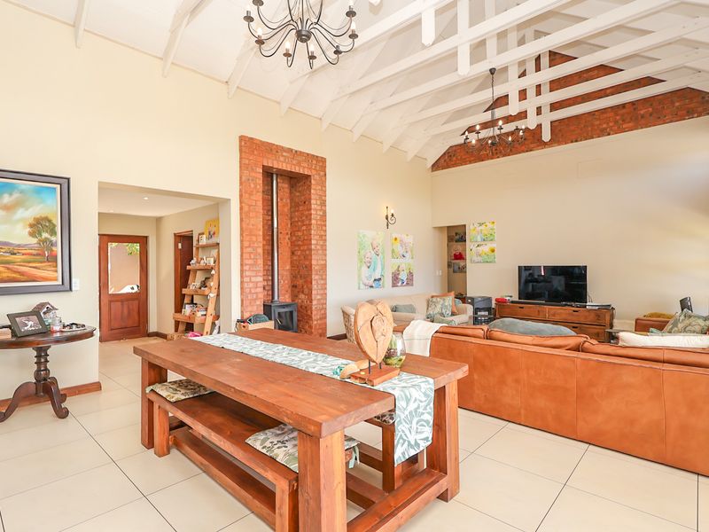 Spacious open-plan living area featuring high vaulted ceilings with exposed timber trusses, tiled flooring, and a prominent exposed brick fireplace.