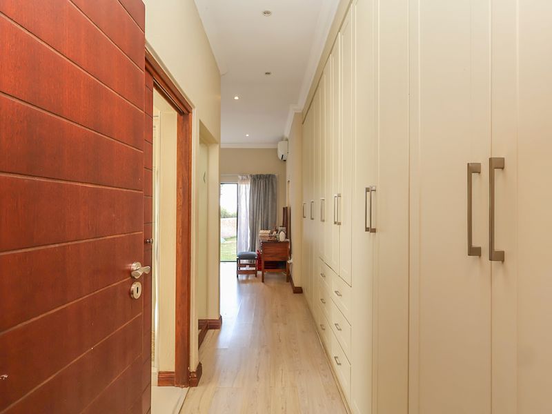 A well-lit hallway featuring extensive built-in cabinetry, laminate flooring, and recessed lighting, leading towards an exterior access point.