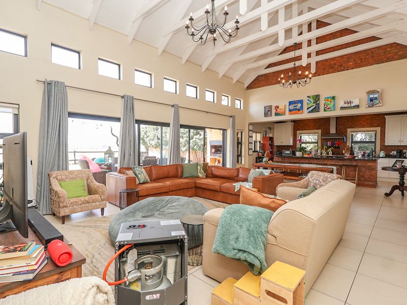 Spacious open-plan living area featuring a vaulted ceiling with exposed trusses, brick accents, tiled floors, and seamless flow to the outdoor patio.