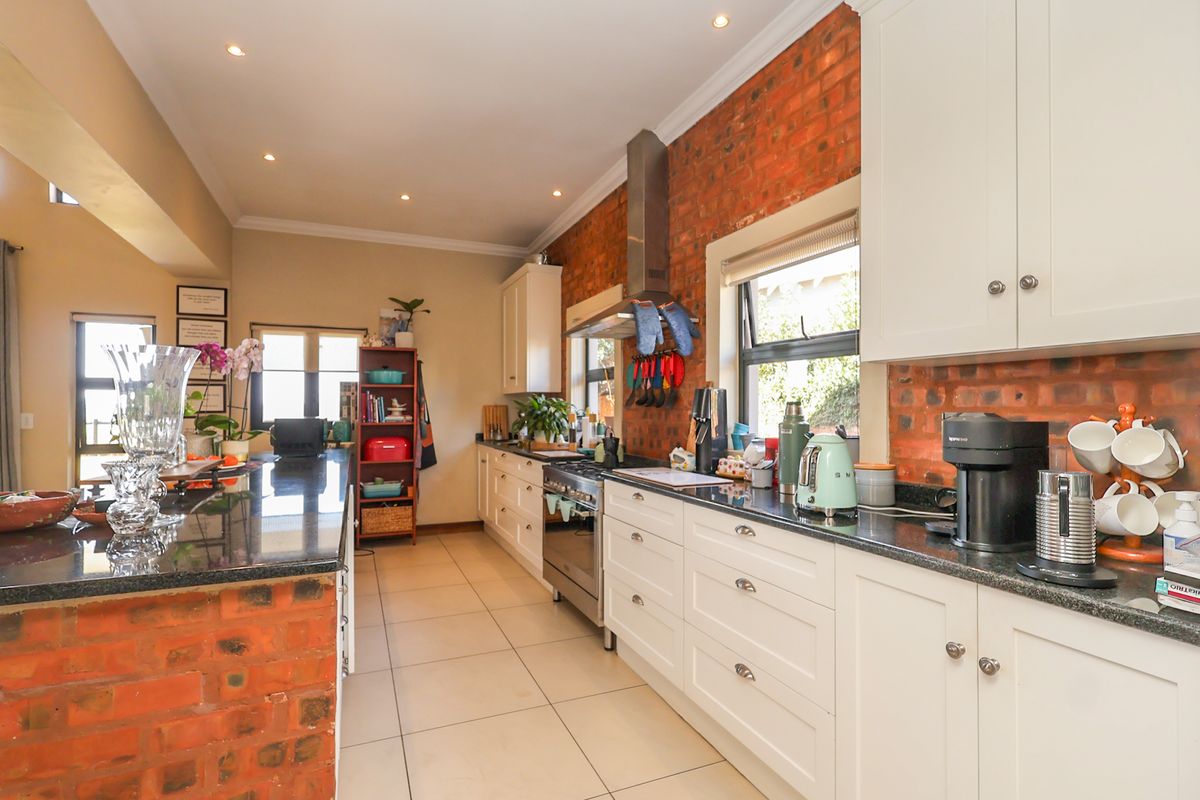 A well-appointed kitchen featuring granite countertops, white cabinetry, and a striking exposed brick feature wall, complemented by modern stainless steel appliances and recessed lighting.