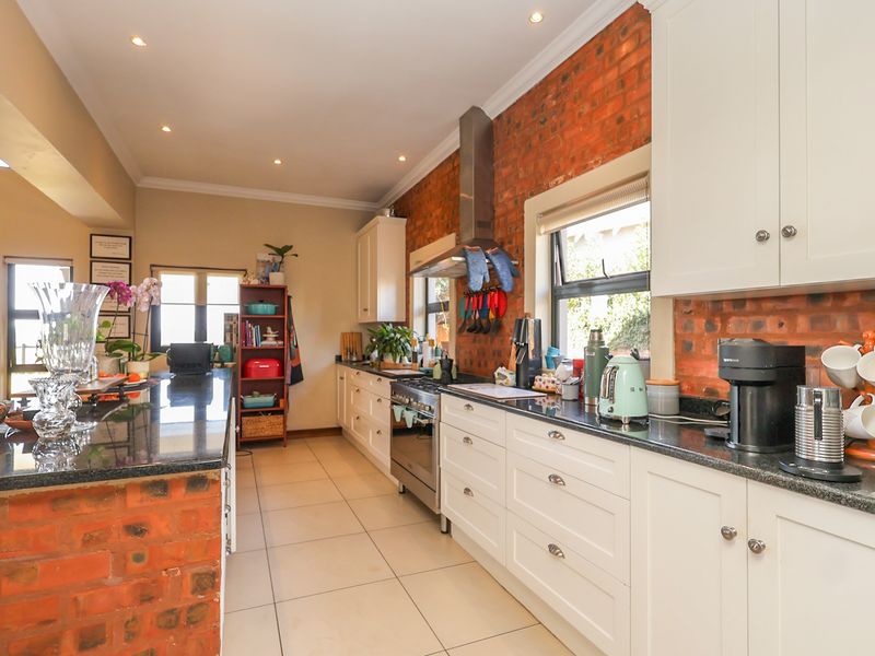 A well-appointed kitchen featuring granite countertops, white cabinetry, and a striking exposed brick feature wall, complemented by modern stainless steel appliances and recessed lighting.