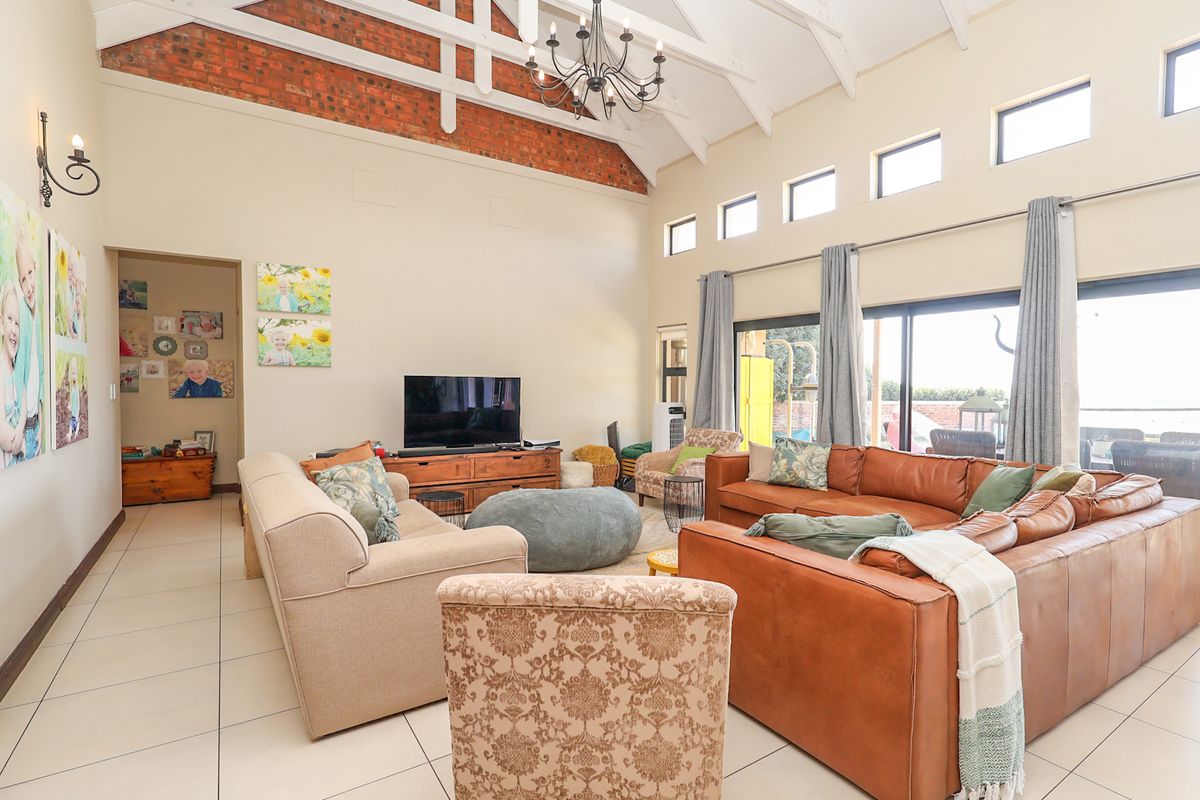 Spacious living room featuring high vaulted ceilings with exposed timber trusses, brick accents, tiled flooring, and large sliding doors providing ample natural light.