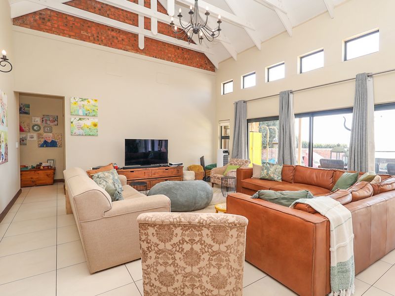 Spacious living room featuring high vaulted ceilings with exposed timber trusses, brick accents, tiled flooring, and large sliding doors providing ample natural light.