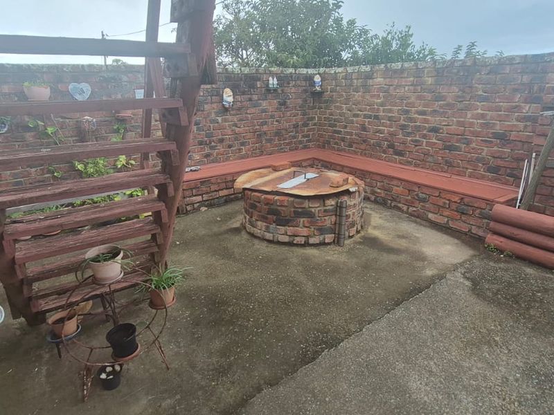 Outdoor patio area featuring a built-in brick fire pit, integrated bench seating, and a wooden staircase enclosed by a brick boundary wall.