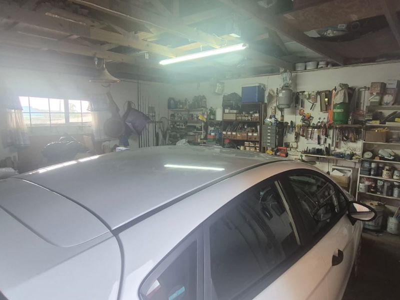 A functional garage space featuring exposed timber roof trusses, fluorescent lighting, and extensive built-in wall shelving for storage.