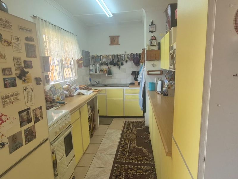 A functional kitchen featuring yellow cabinetry, laminate countertops, a freestanding stove, and tiled flooring, offering a classic layout with ample storage space.