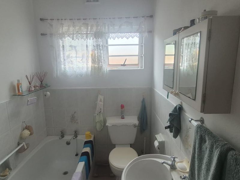 A functional bathroom featuring a standard bathtub, pedestal basin, and toilet with tiled splashbacks and a wall-mounted medicine cabinet.