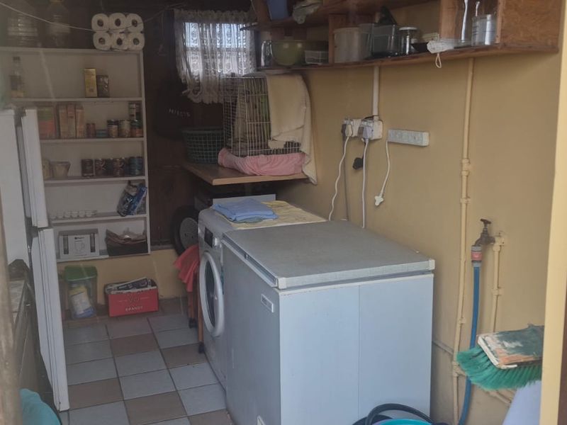 A functional laundry area featuring tiled flooring, built-in shelving, and exposed plumbing connections for appliances.