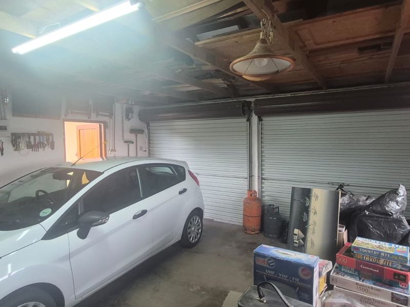 A functional double garage featuring exposed timber ceiling beams, concrete flooring, and dual roller doors, providing ample space for vehicle storage and workshop use.