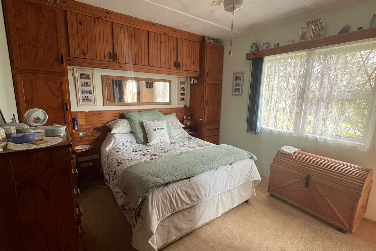 A bedroom featuring extensive built-in wooden cabinetry, a ceiling fan, and a window fitted with a security gate.