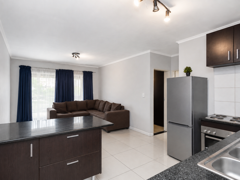 Open-plan living area featuring a modern kitchen with granite countertops, dark wood cabinetry, and tiled flooring, seamlessly flowing into the adjacent living space.