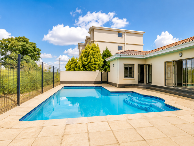 A well-maintained outdoor pool area featuring a clear swimming pool, tiled decking, and direct access to the apartment through sliding glass doors.