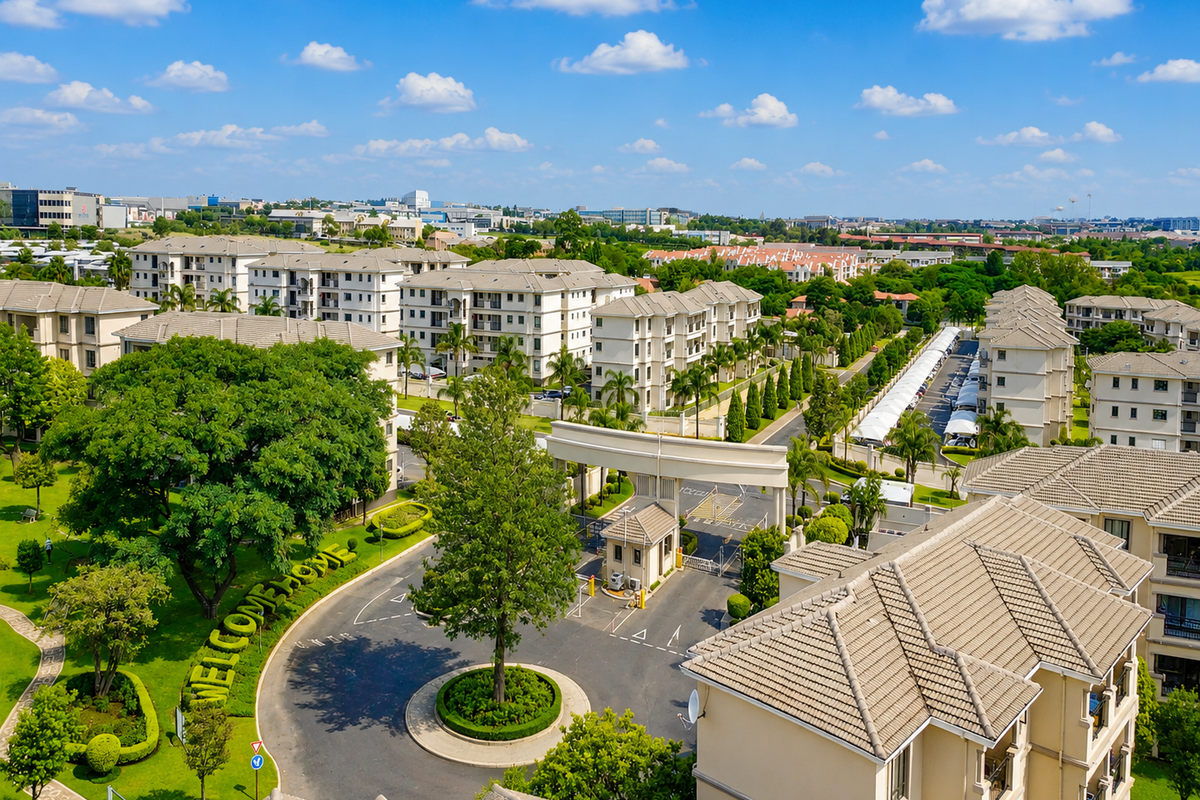 Aerial view of a well-maintained residential apartment complex featuring landscaped grounds, a secure gated entrance, and paved internal access roads.