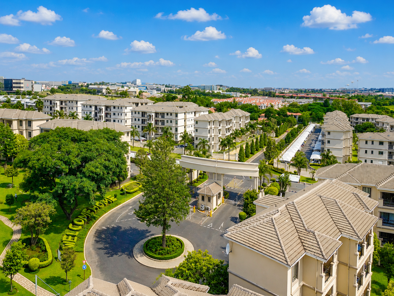 Aerial view of a well-maintained residential apartment complex featuring landscaped grounds, a secure gated entrance, and paved internal access roads.