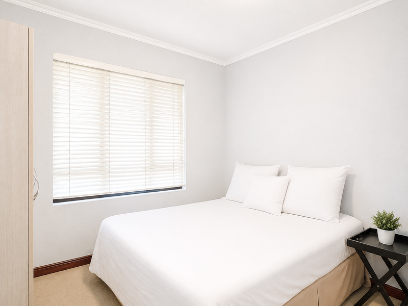 A clean and bright bedroom featuring neutral walls, carpeted flooring, a built-in wardrobe, and venetian blinds for privacy.