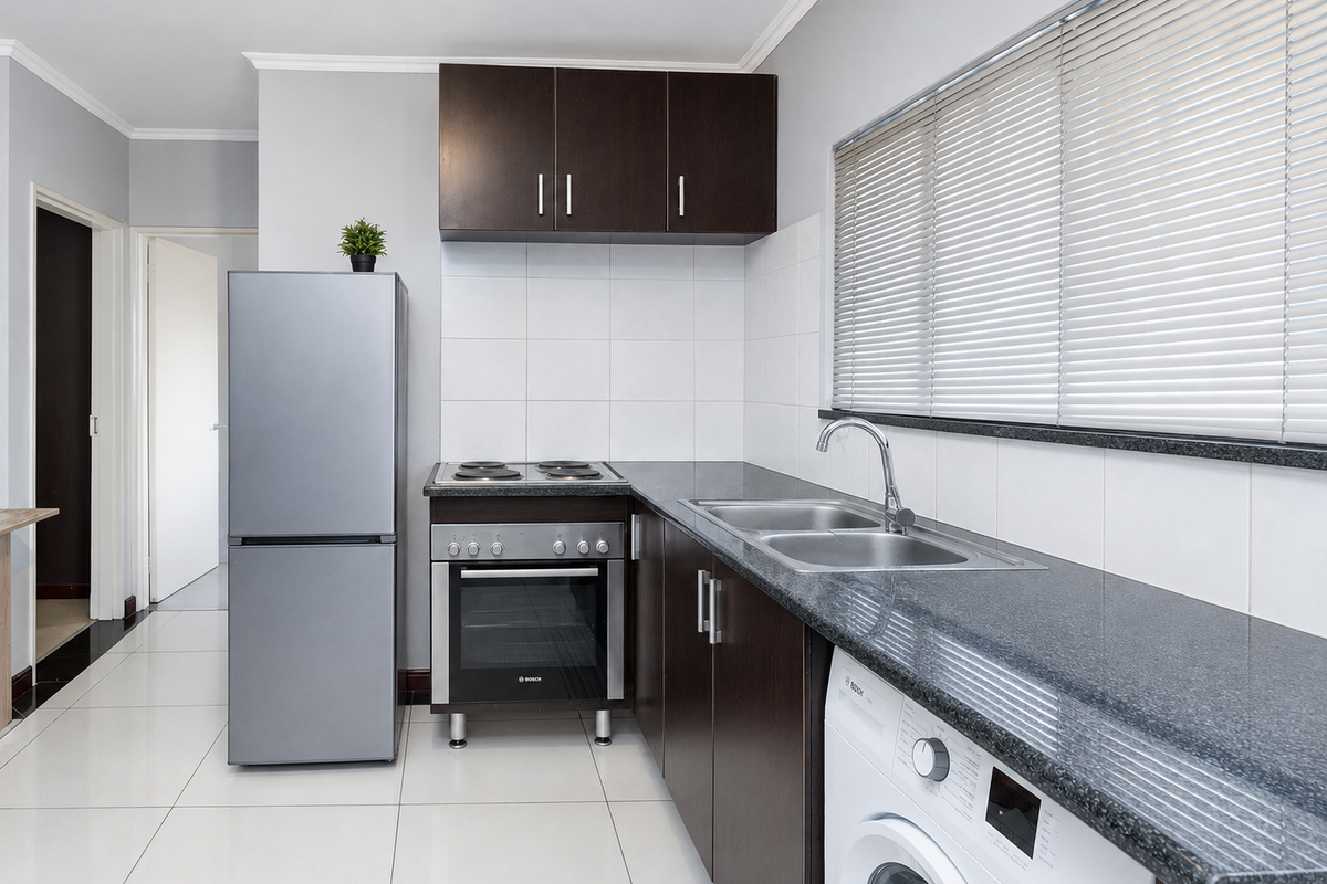 A functional kitchen featuring dark wood cabinetry, granite countertops, a stainless steel sink, and built-in oven with electric hob.