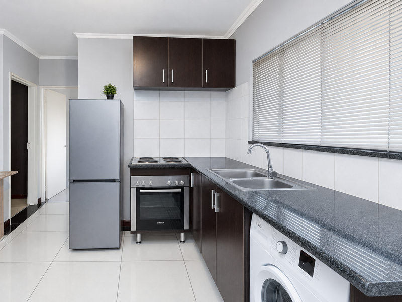 A functional kitchen featuring dark wood cabinetry, granite countertops, a stainless steel sink, and built-in oven with electric hob.