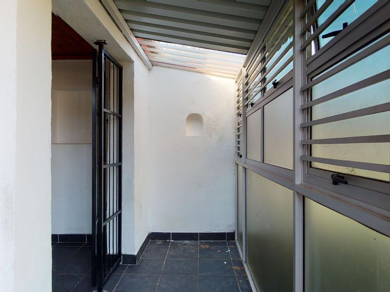 A covered patio area featuring tiled flooring, a metal security gate, and louvre windows, providing a functional outdoor transition space.