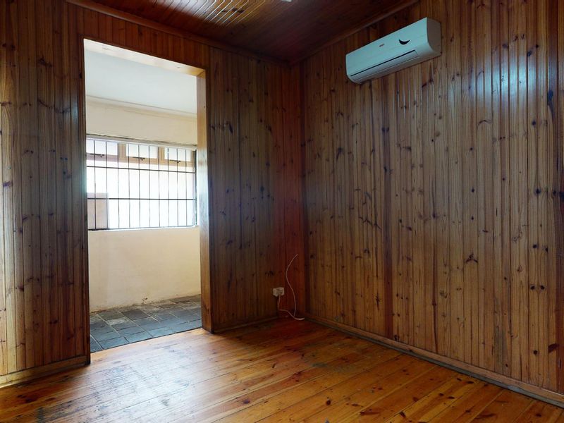 An empty bedroom featuring extensive timber wall paneling, timber ceiling, and timber flooring, equipped with a wall-mounted air conditioning unit.